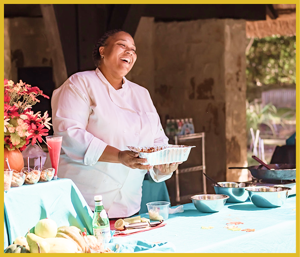 Chef joyfully presenting dishes at an outdoor event with a vibrant, colorful setup.