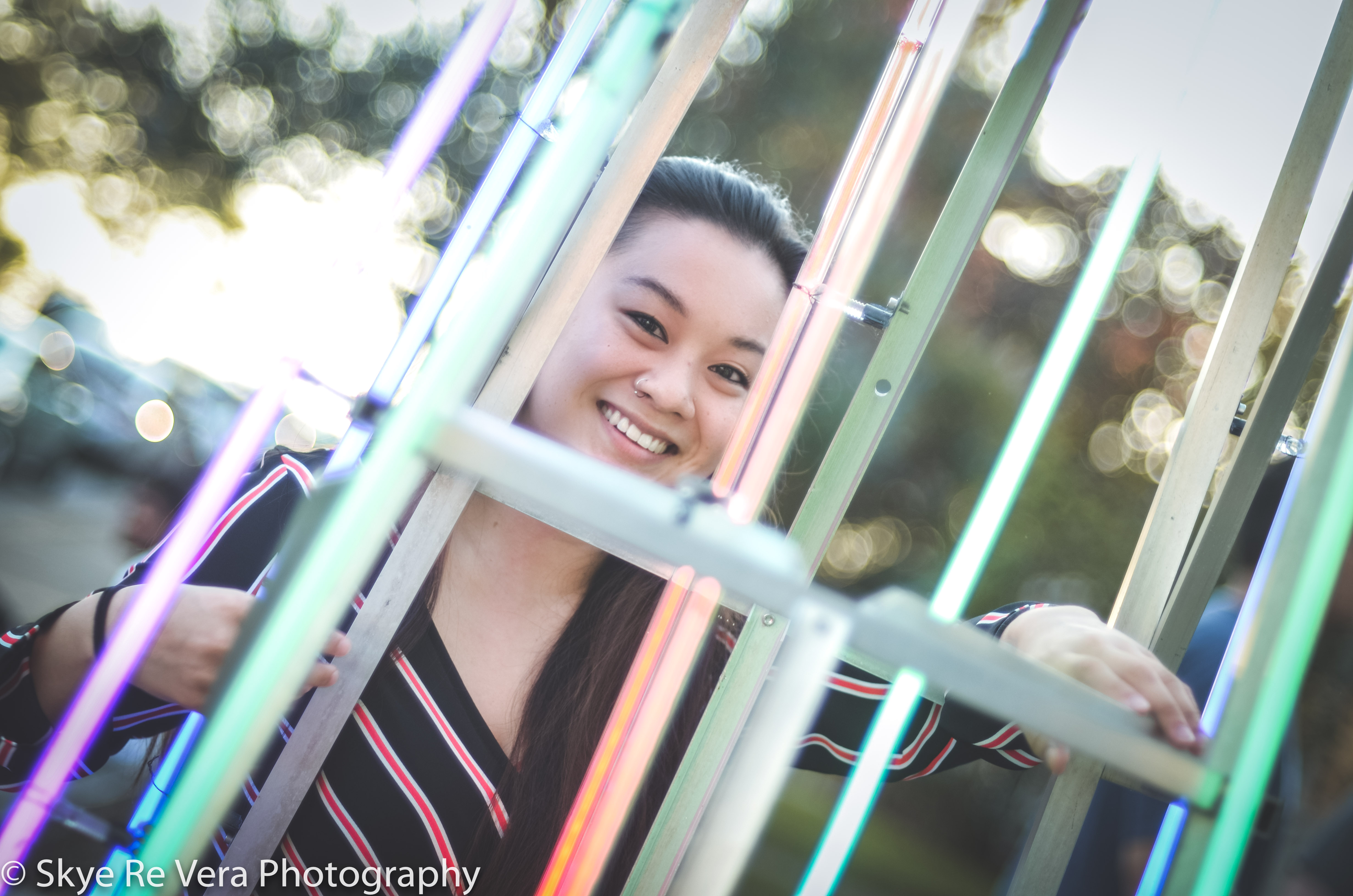 Person smiling with colorful lights, outdoors, evening setting.