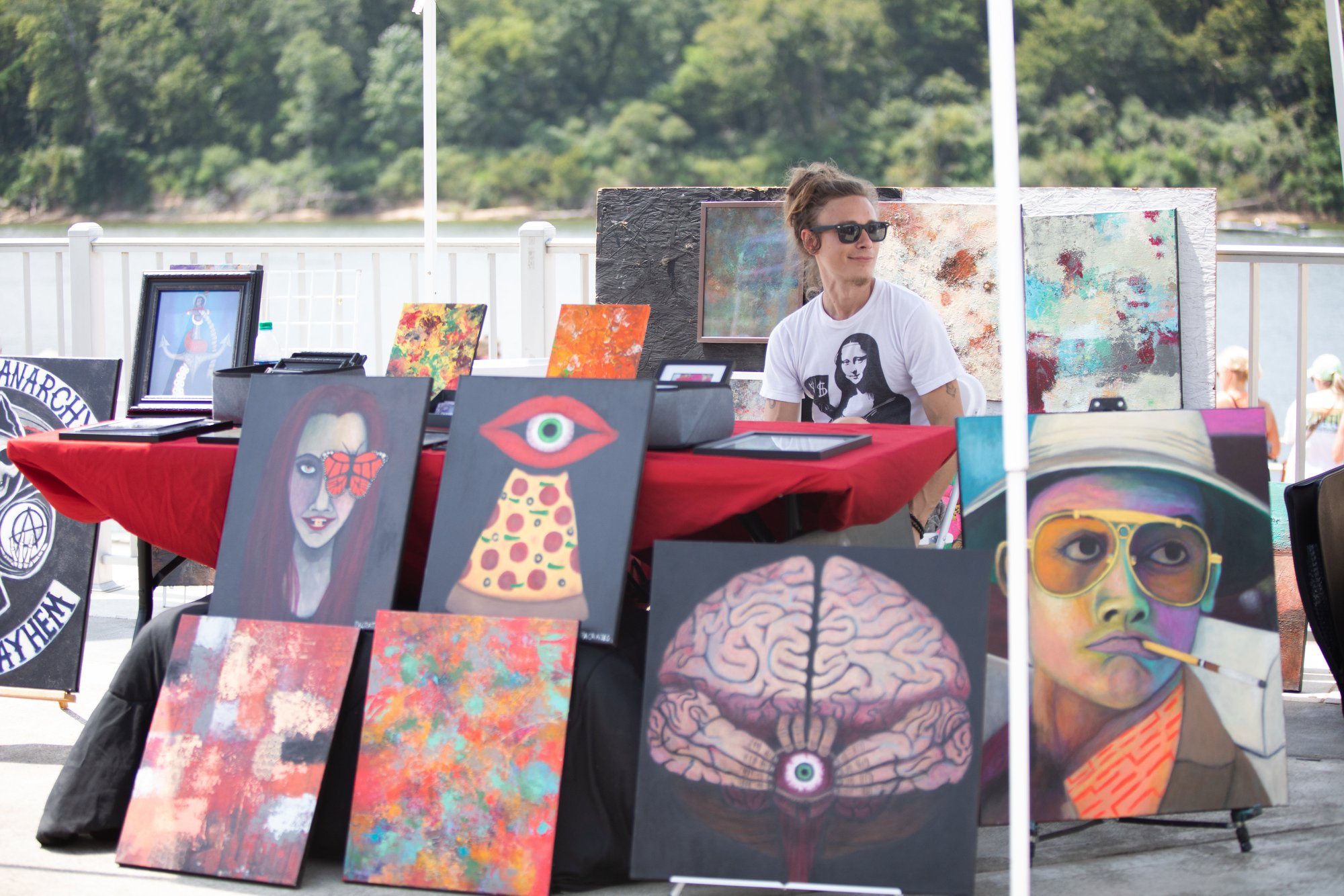 Artist painting outdoors with vibrant artwork in the background.