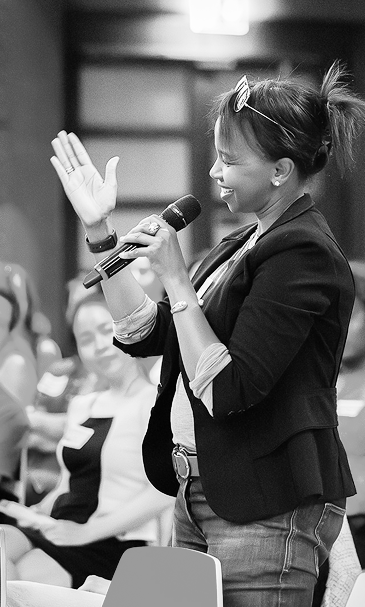 Black and white photo of a Hello 50 50 World ambassador speaking on stage with a microphone at one of our events.