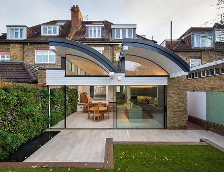 Modern living space with curved glass roof connecting traditional house to garden with exterior living wall