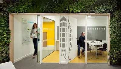 Living wall surrounds modern office pods with yellow and white workspace