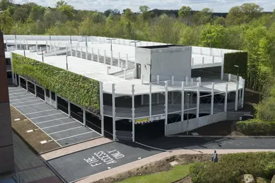 Modern living building with green wall amid lush trees and parking area