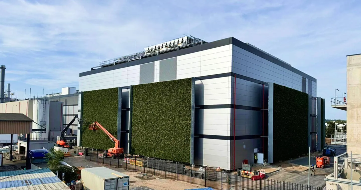 Living green wall covers modern industrial building with construction equipment