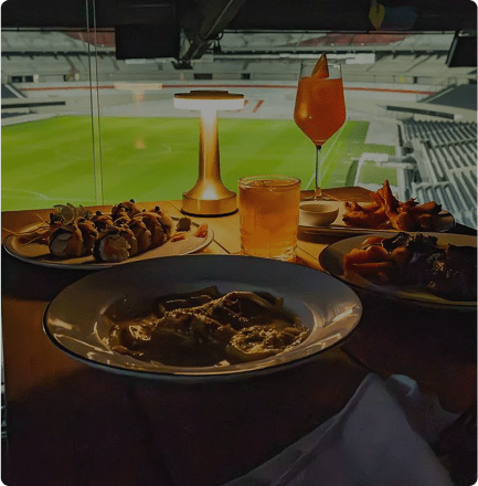 Mesa con platos de comida y bebidas con vista al estadio Monumental