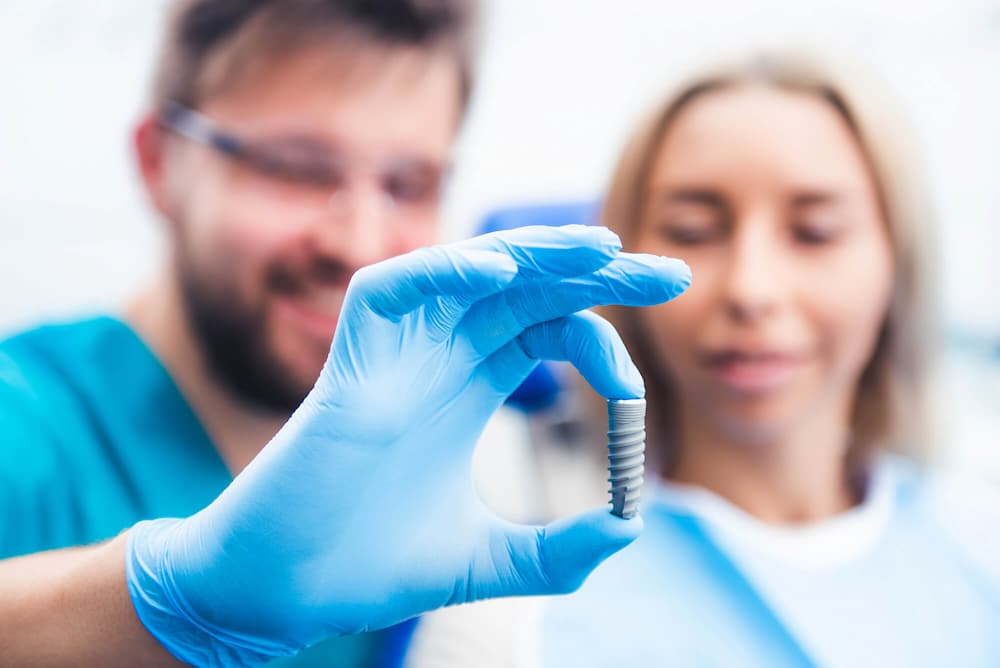 photo of a dentist holding a dental implant post and showing it to a female patient
