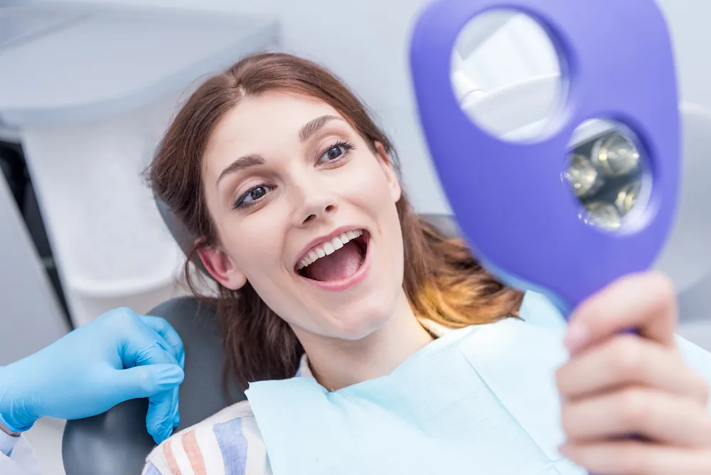 photo of a happy female patient looking in the mirror and loving her smile
