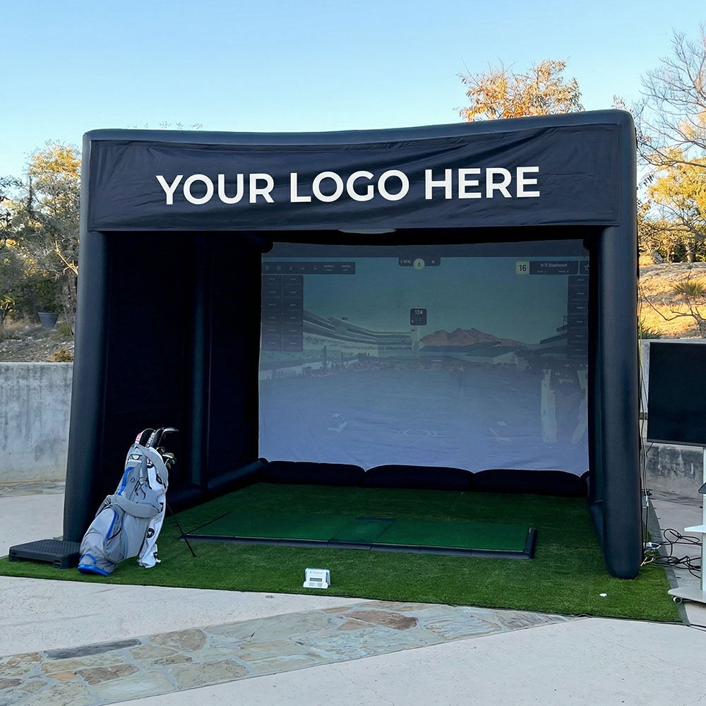 Outdoor golf simulator setup with a black inflatable enclosure labeled 'YOUR LOGO HERE' and a golf bag nearby.