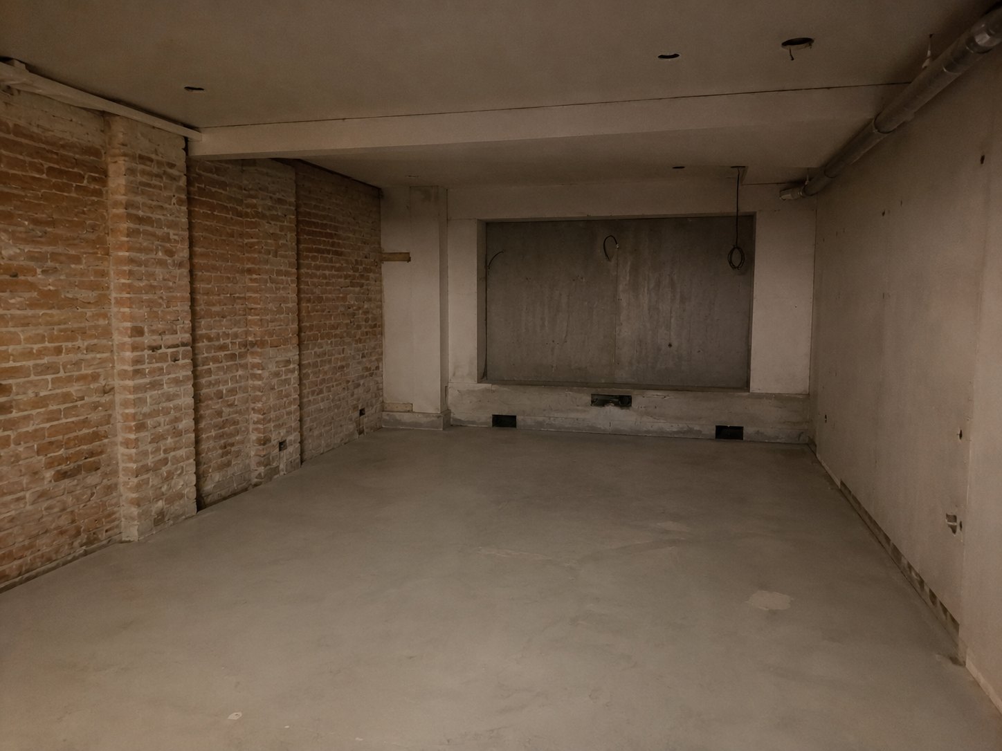 Lower-ground room in a Sydney terrace house before acoustic conversion, showing existing masonry walls, concrete floor and unfinished ceiling structure.