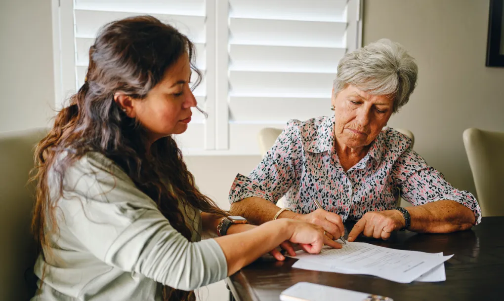 A daughter an mother sitting at a table reviewing powers of attorney documents