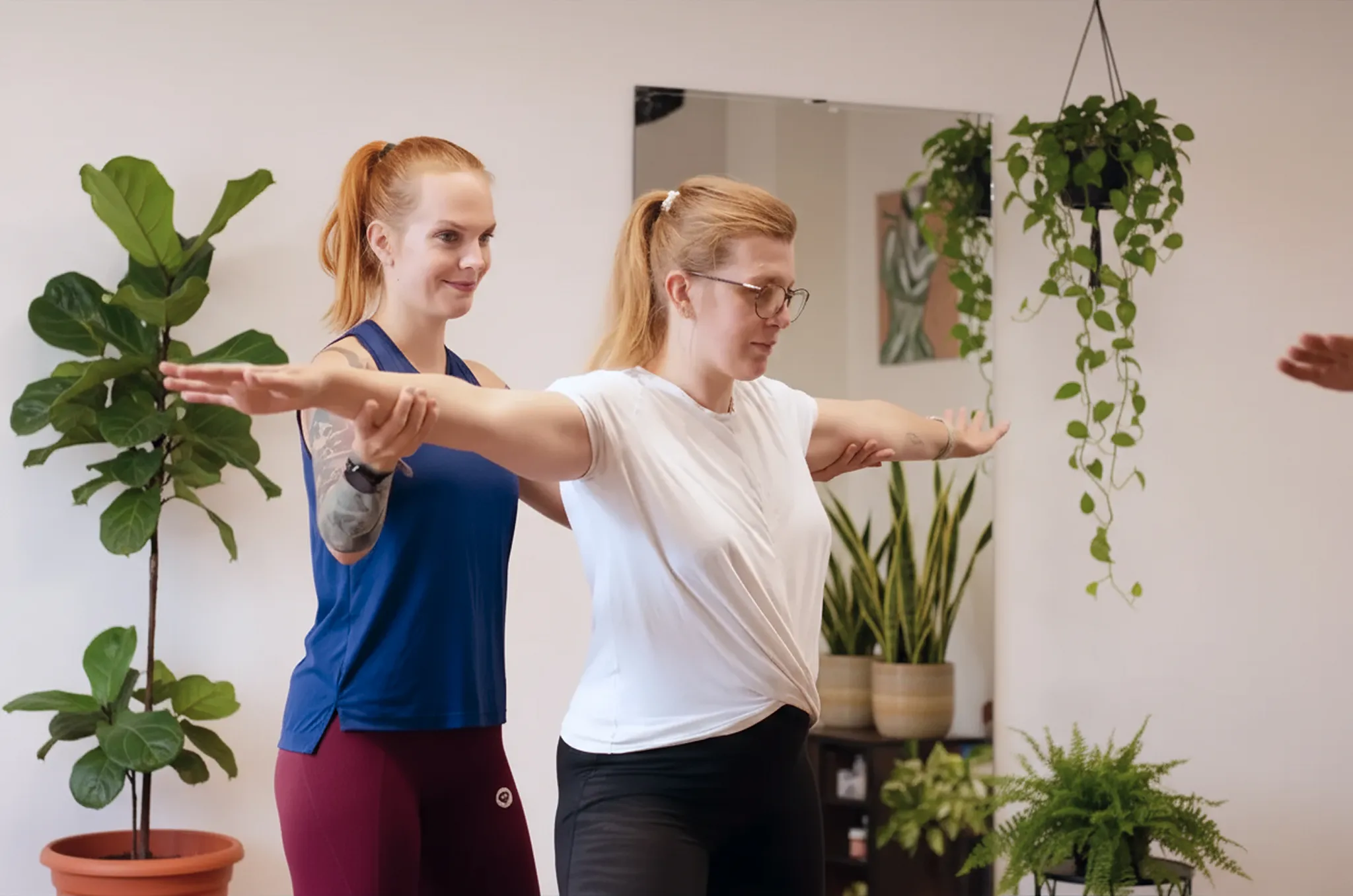 Dve ženy cvičia vo fitnescentre, jedna pomáha druhej udržať rovnováhu.