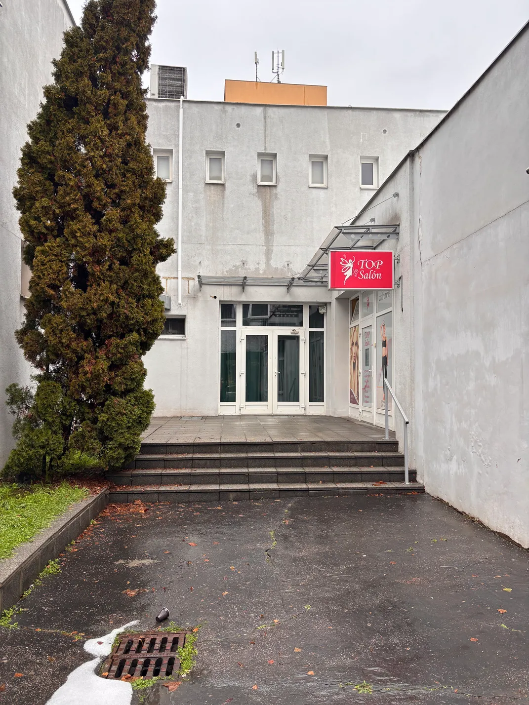 Vchod do budovy s červeným označením Top Salón vedľa veľkého stromu a niekoľkými schodmi.
