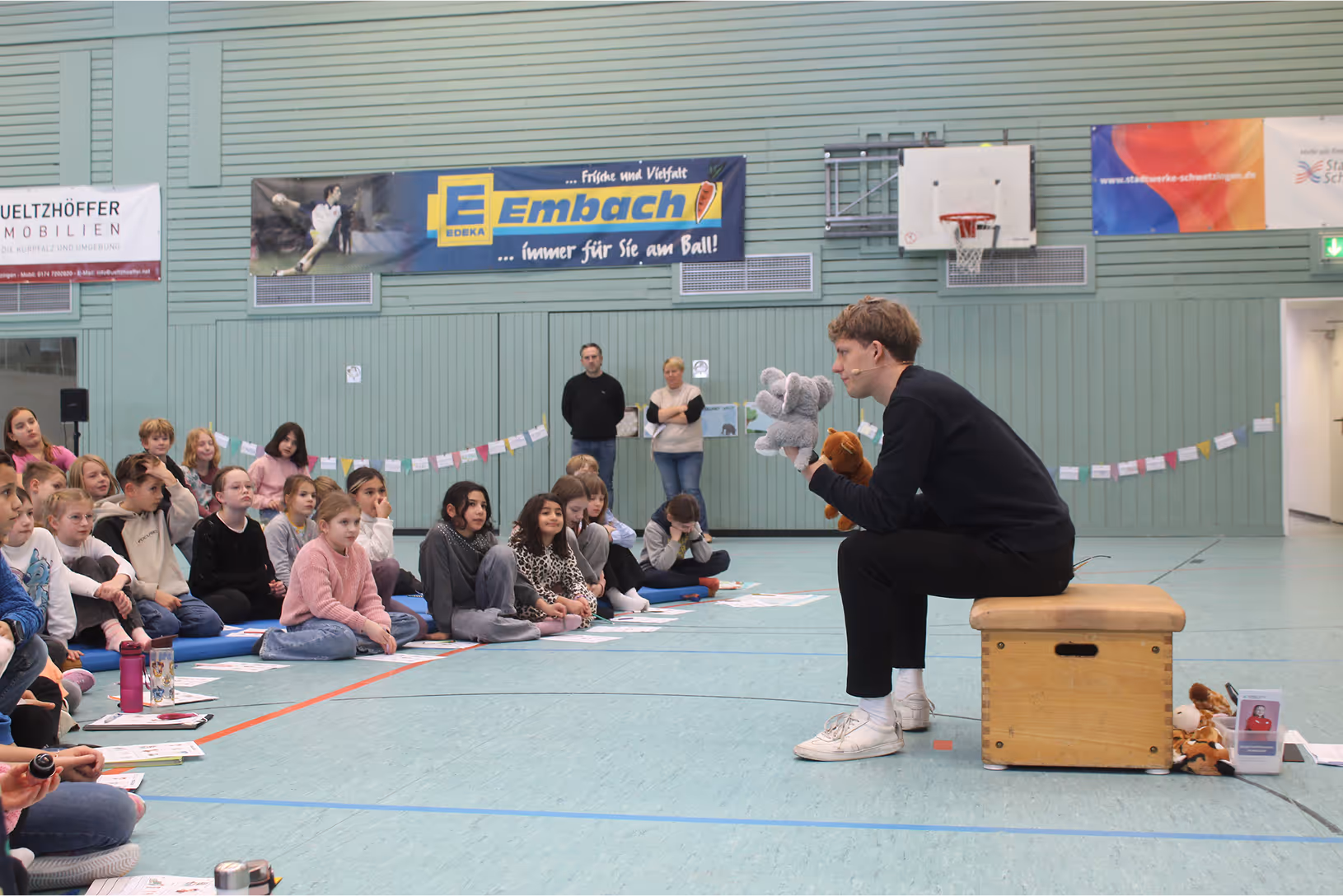 A teacher holding a stuffed animal in front of a crowd of people.