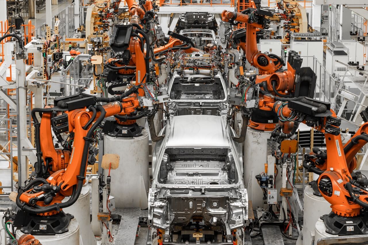 Automobilfertigungslinie mit mehreren orangen Industrierobotern, die Karosserien von Fahrzeugen montieren.