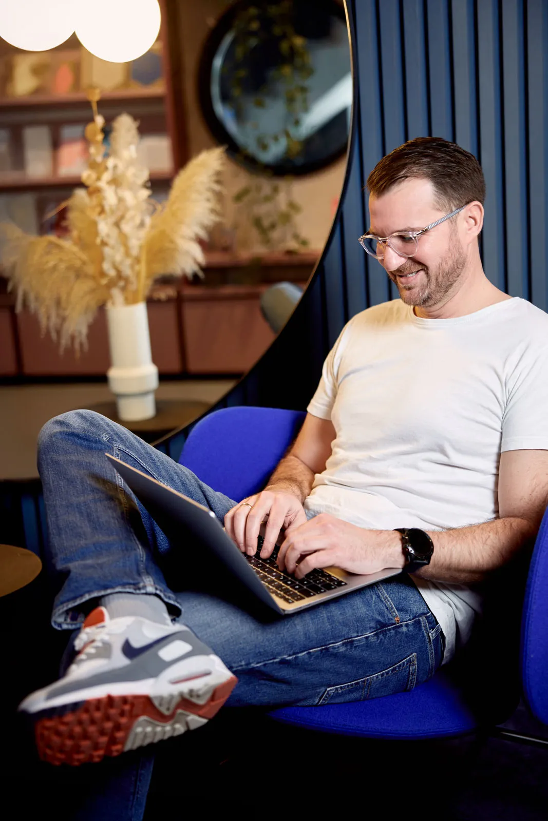 Philip Fuchslocher sitzt in einem blauen Sessel und lächelt, während er in den Laptop tippt