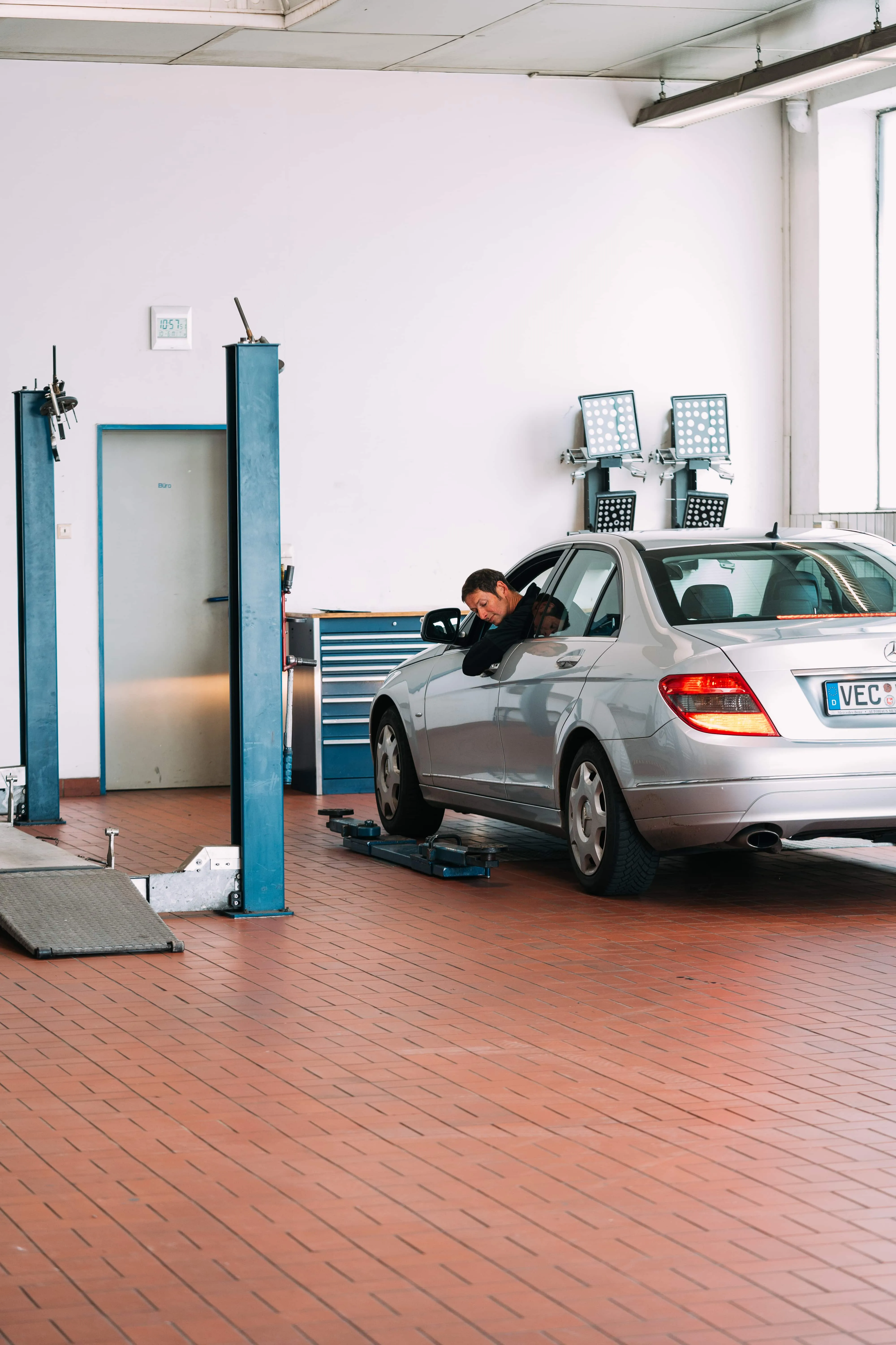 Silberne Mercedes-Benz C-Klasse in der Werkstatt, Mitarbeiter schaut aus dem Fahrerfenster