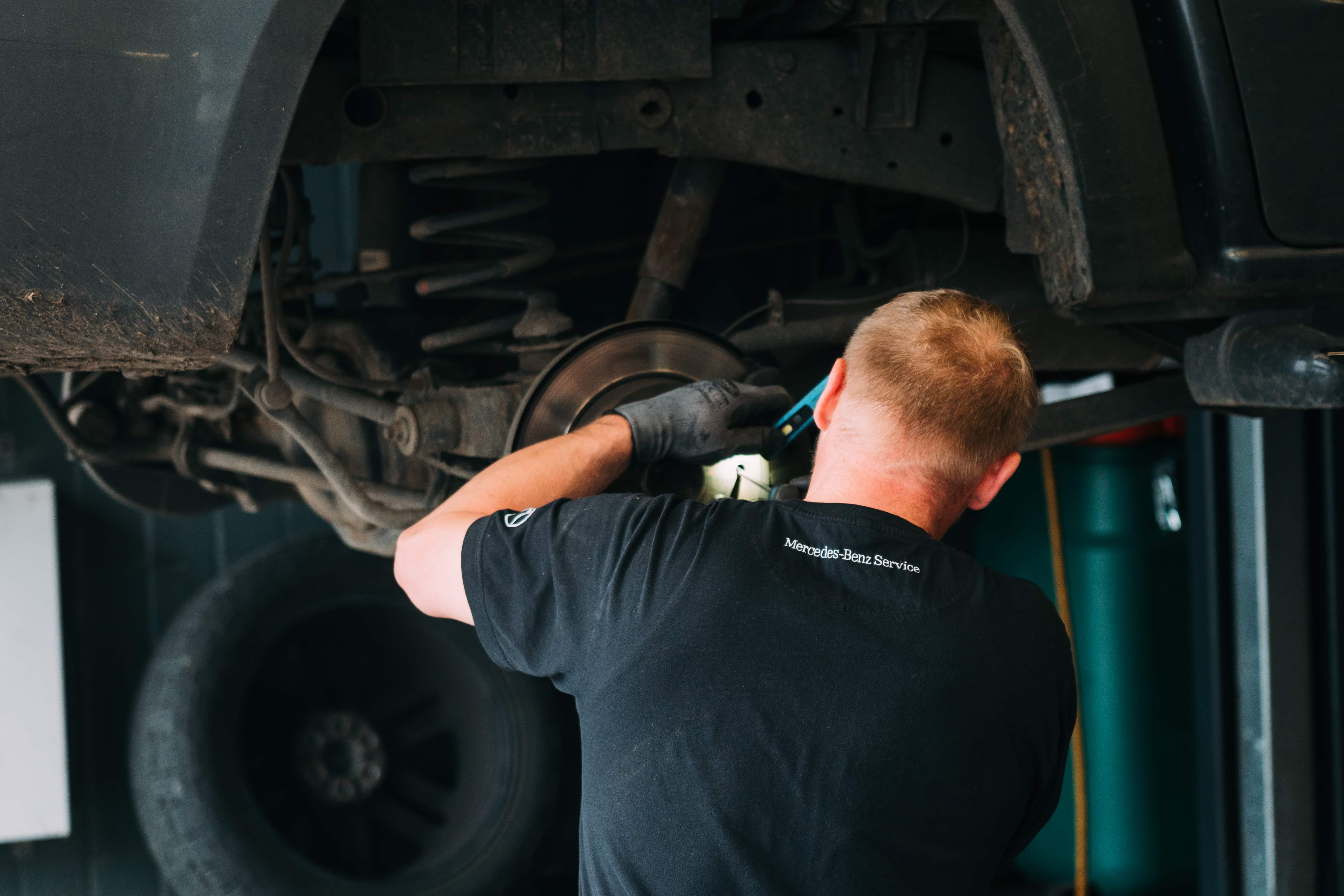Mechaniker in Mercedes-Benz Service Kleidung arbeitet am Fahrwerk eines Fahrzeugs