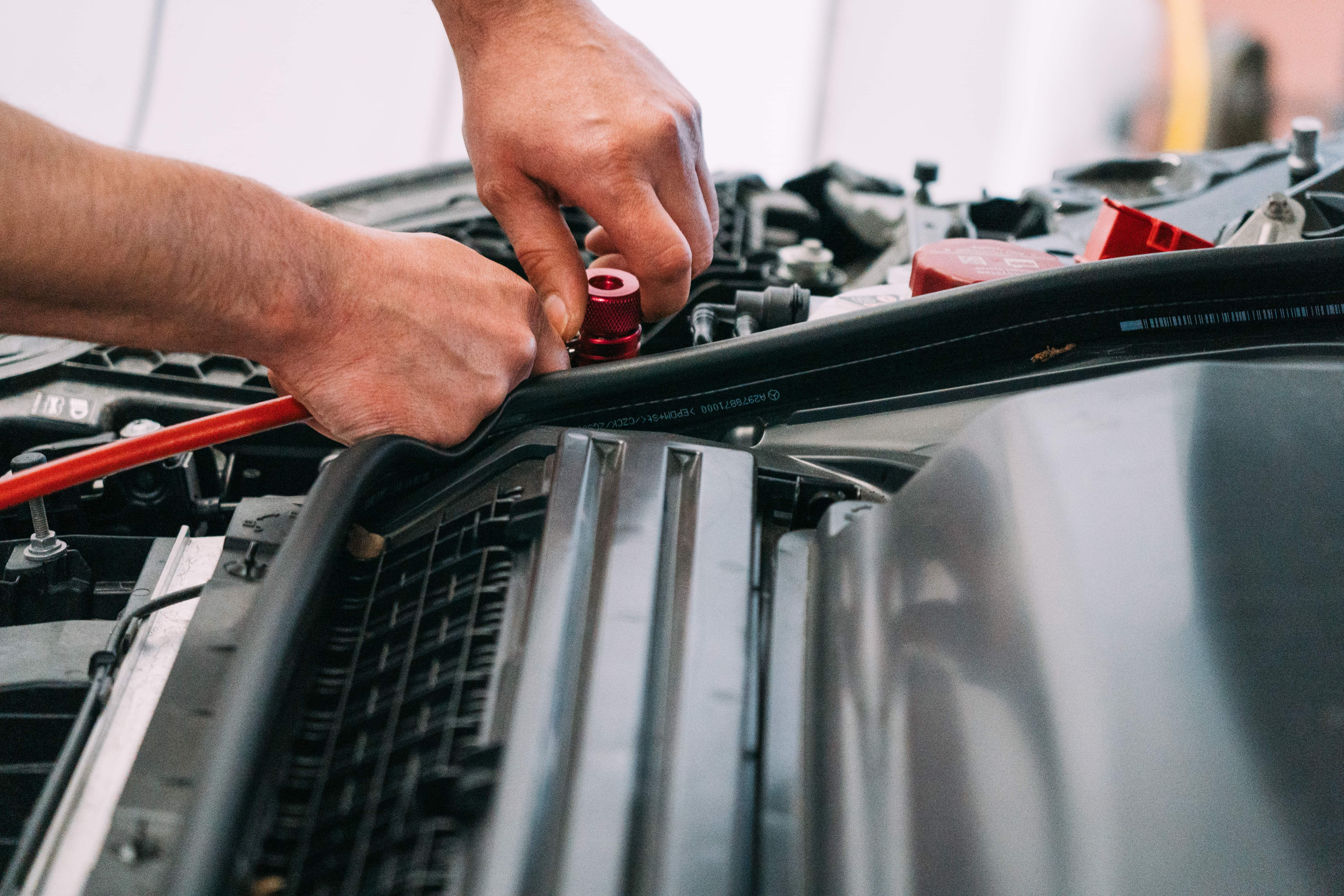 Hände eines Mechanikers schließen ein Kabel an die Fahrzeugbatterie an