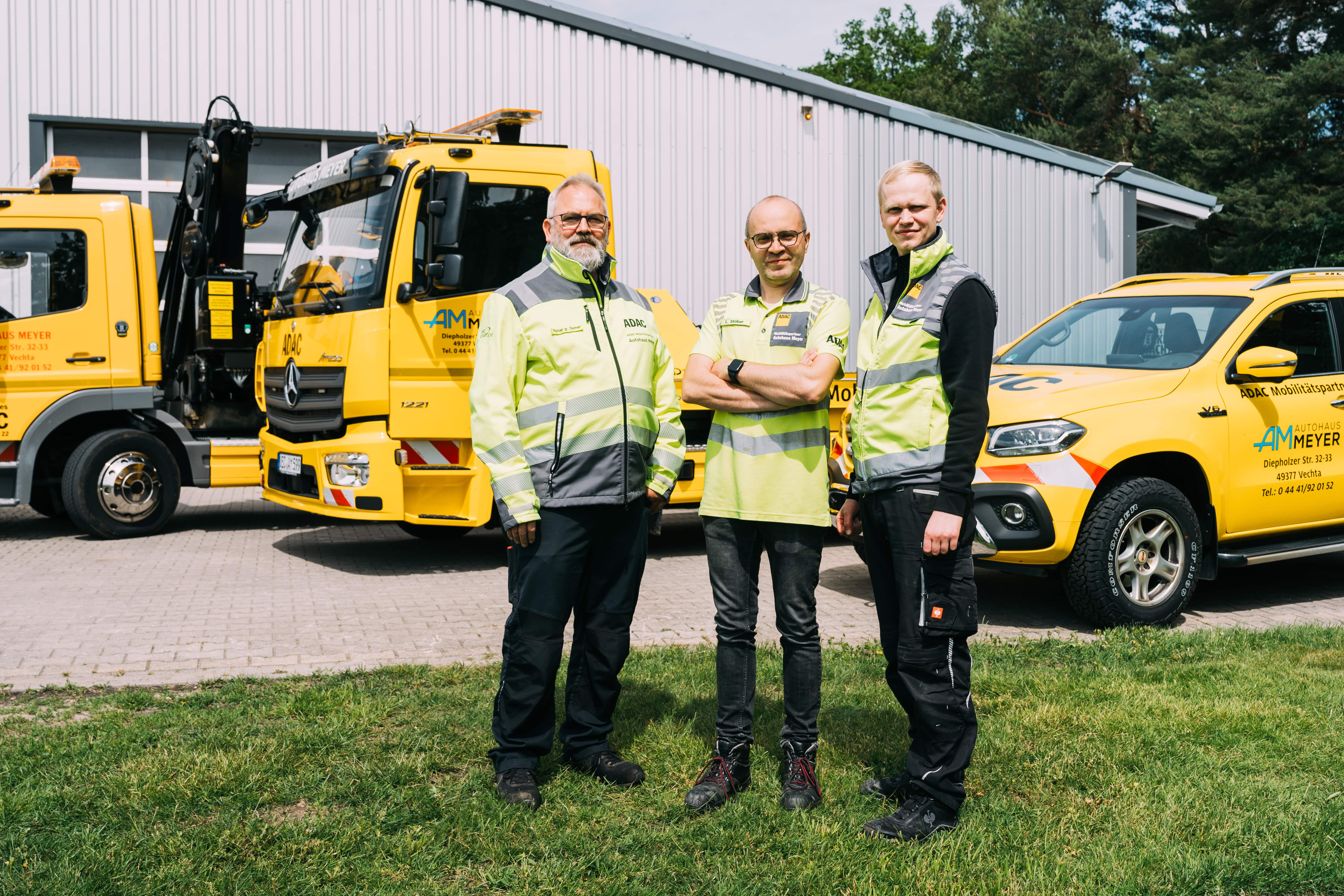 Drei Mitarbeiter des Pannen- und Abschleppdienstes in Warnwesten vor den Abschleppfahrzeugen