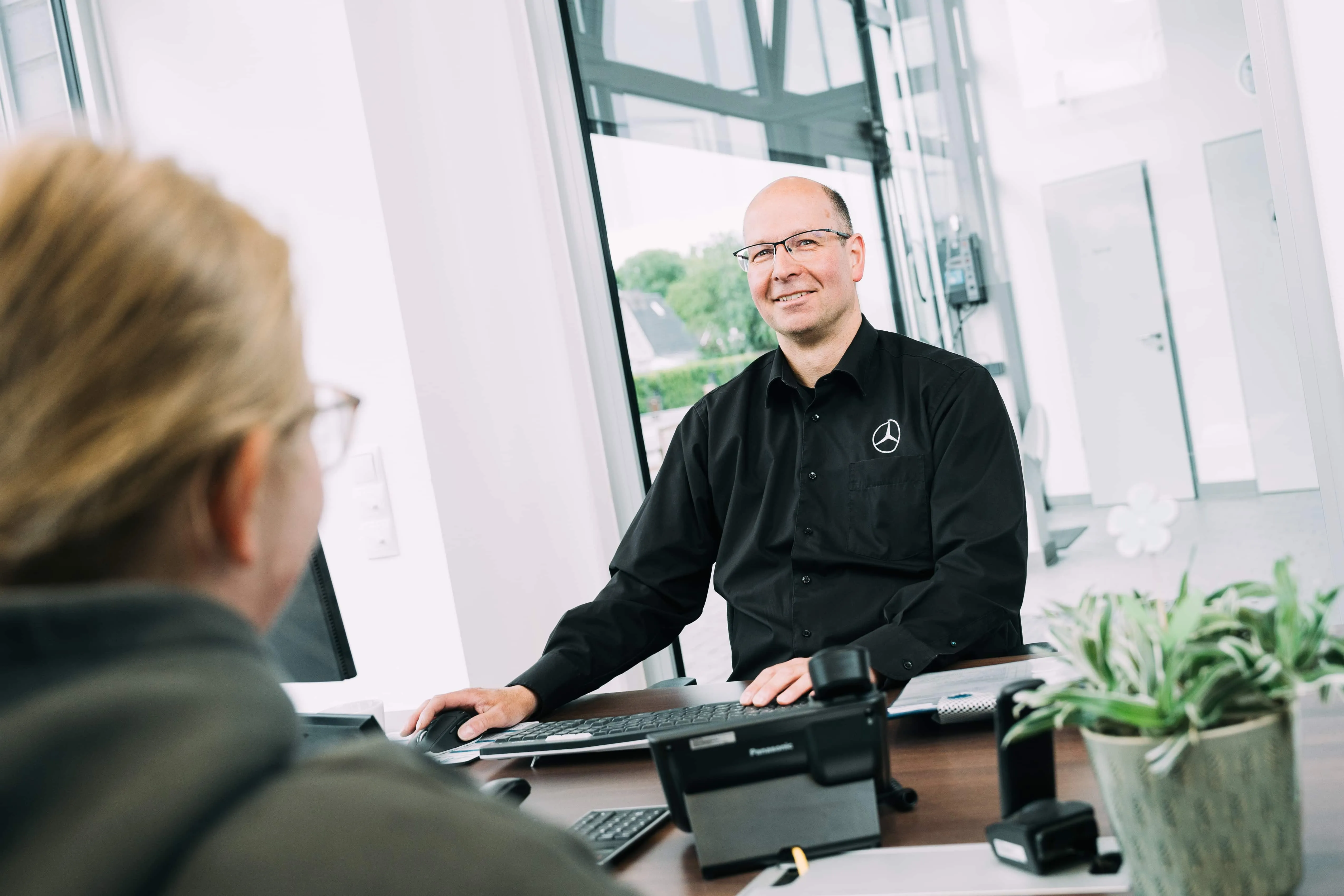 Mitarbeiter von Autohaus Meyer berät eine Kundin am Schreibtisch