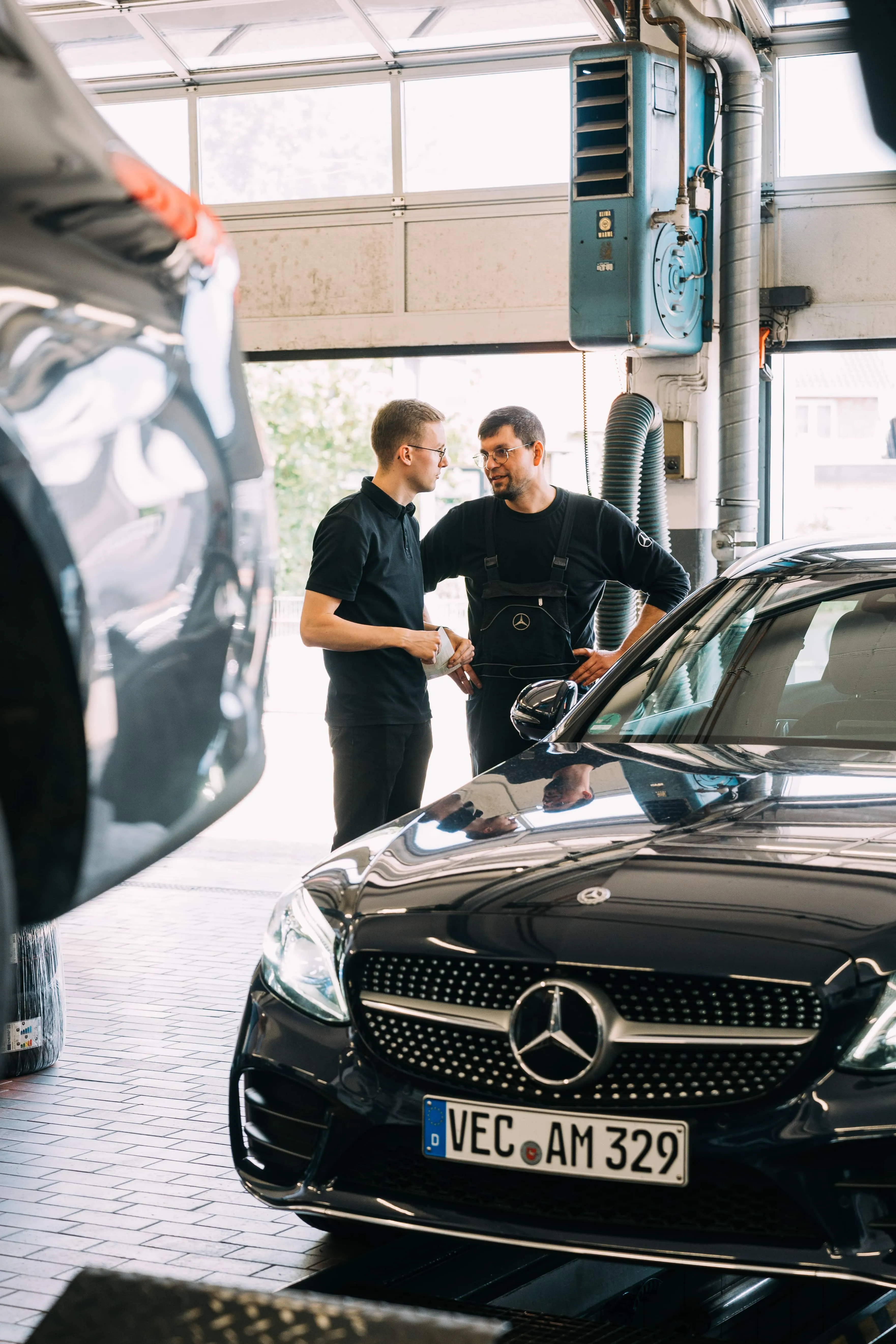 Serviceberater und Mechaniker besprechen sich in der Werkstatt neben einem Mercedes-Benz