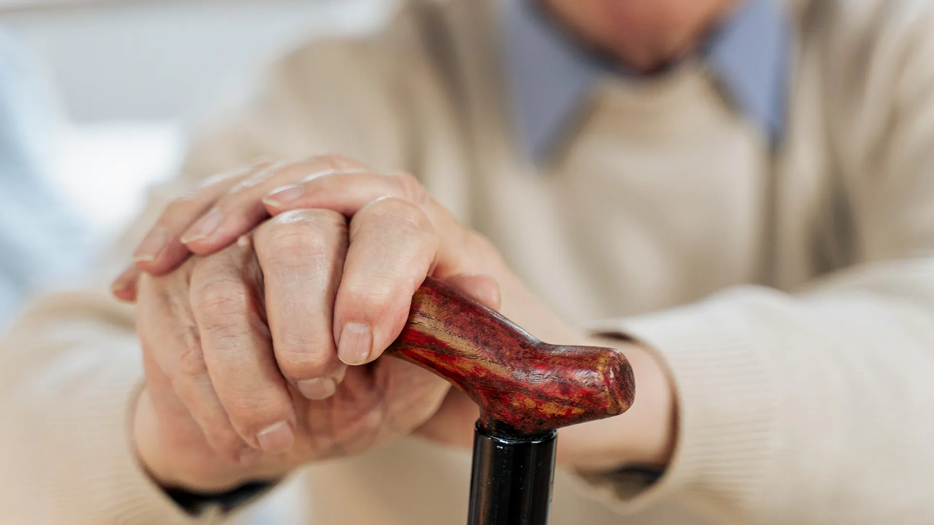 Hände eines älteren Menschen, die einen Holzstock umklammern.