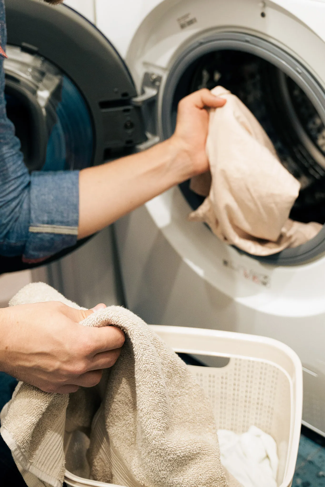 Person legt Kleidung in eine Frontlader-Waschmaschine und hält einen Handtuchkorb.