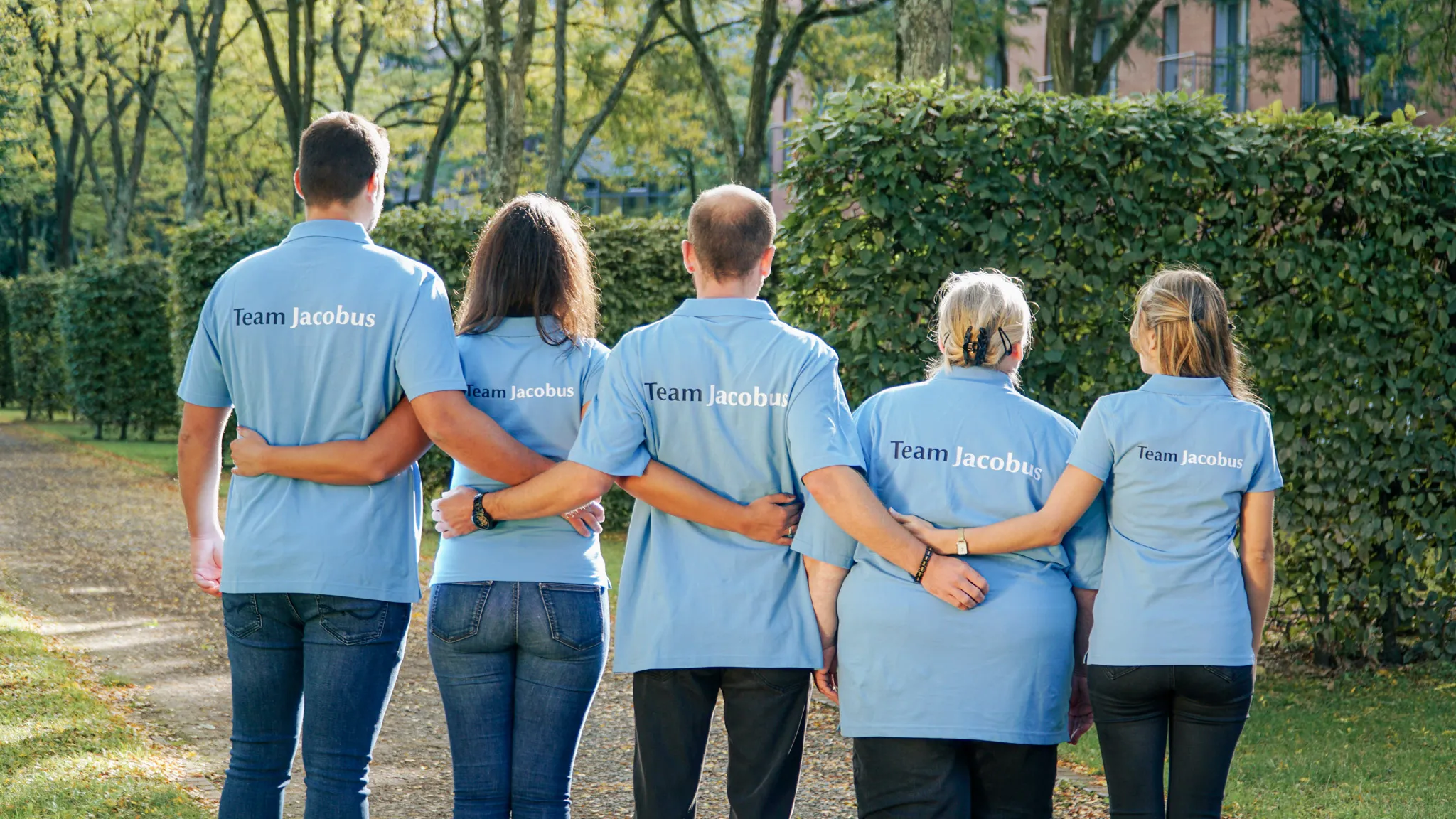 Fünf Personen mit blauen Poloshirts, auf denen Team Jacobus steht, stehen nebeneinander mit verschränkten Armen im Freien.
