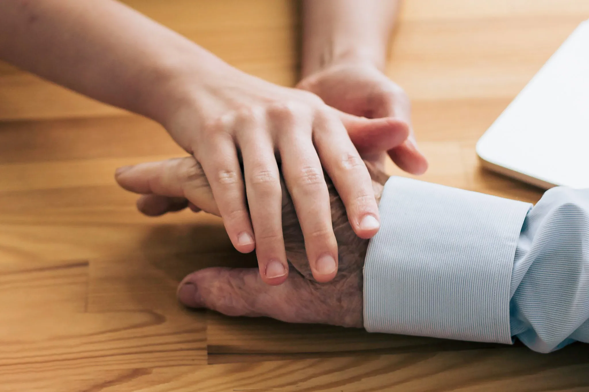 Junge Hand hält fürsorglich die Hand eines älteren Menschen auf einem Holztisch.