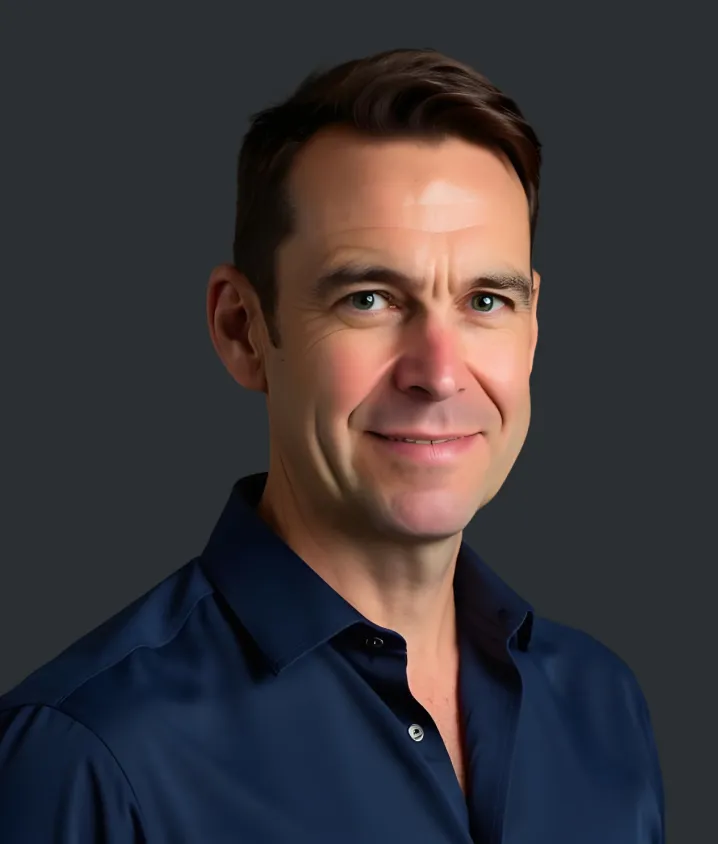 Portrait of a man with short brown hair wearing a dark blue button-up shirt against a dark background. Ed Richards