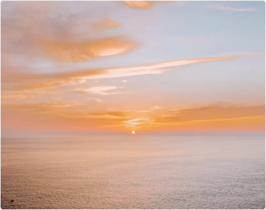 The sun is setting over the ocean on a cloudy day.