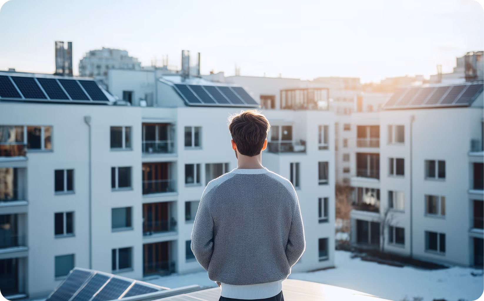Mann schaut entspannt auf moderne Mehrfamilienhäuser mit Solaranlagen im Sonnenschein (Symbolbild). Alle Informationen zum Solarspitzengesetz 2025 im metergrid Blog.