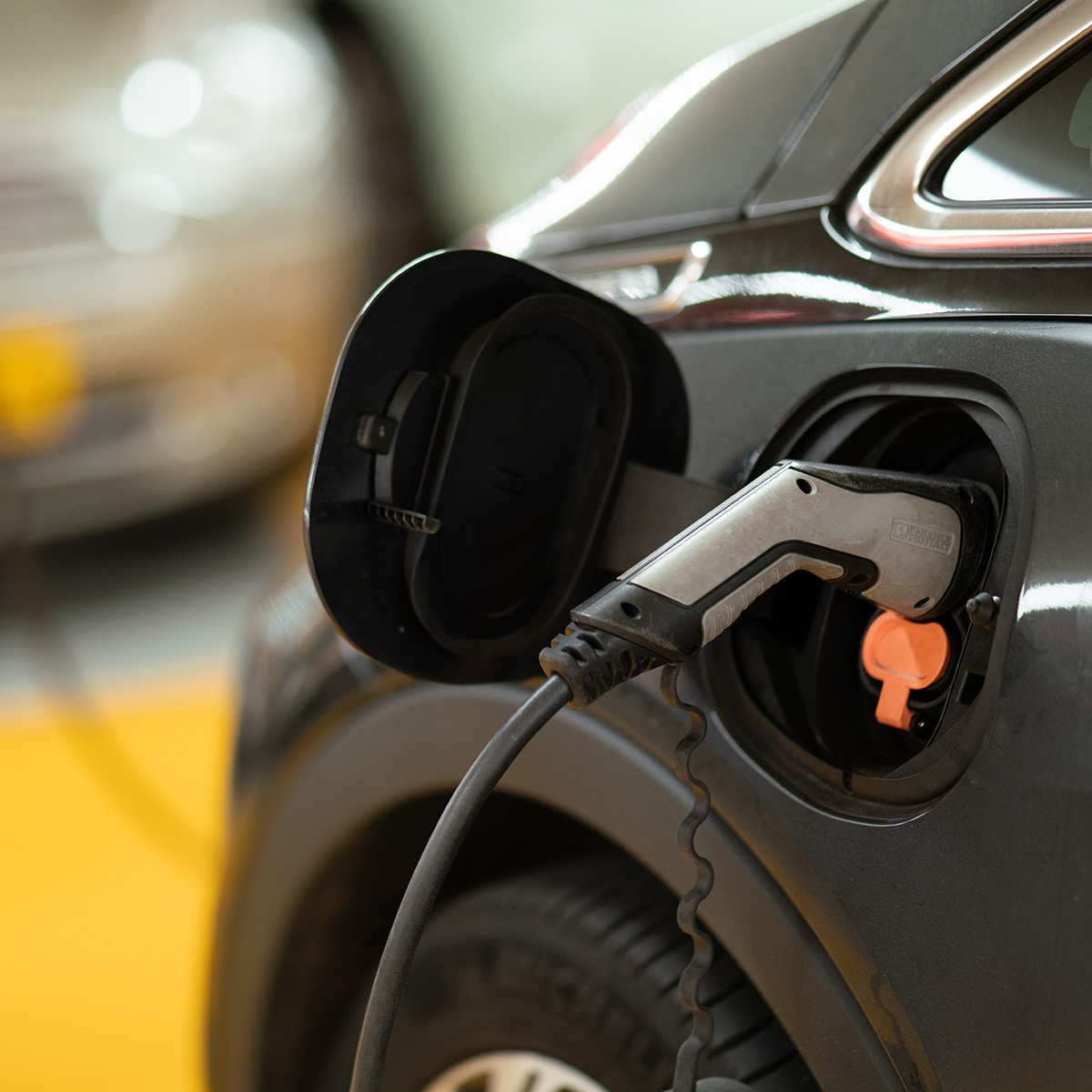 A black electric car being charged, with the charging cable connected to its port, indicative of sustainable transportation technology.