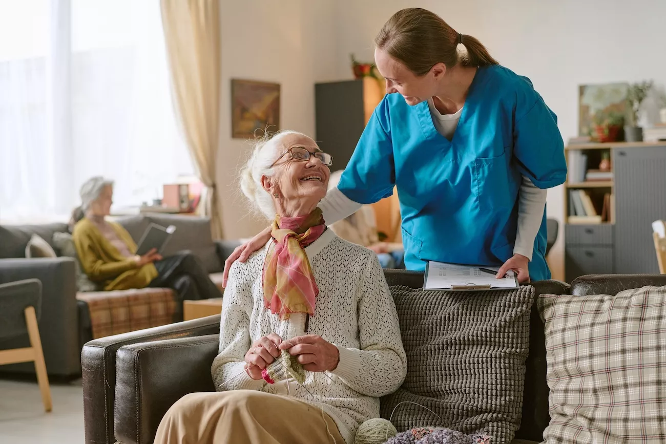 Care home carer checking in with an elderly resident in a shared living space, reflecting the continuous occupancy that shapes legionella compliance in care settings