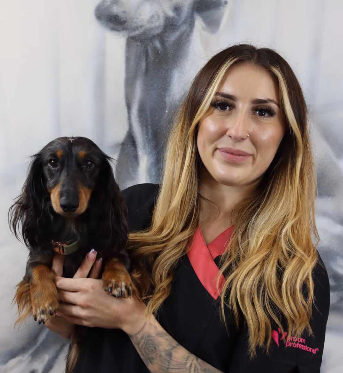 Smiling woman with long blonde hair holding a black and tan dachshund dog.