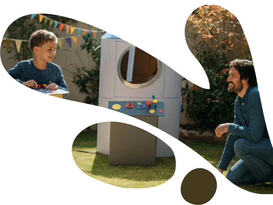 A father watching his young son play at a colorful outdoor playground structure with a spaceship design, both wearing matching blue shirts in a warm, natural setting