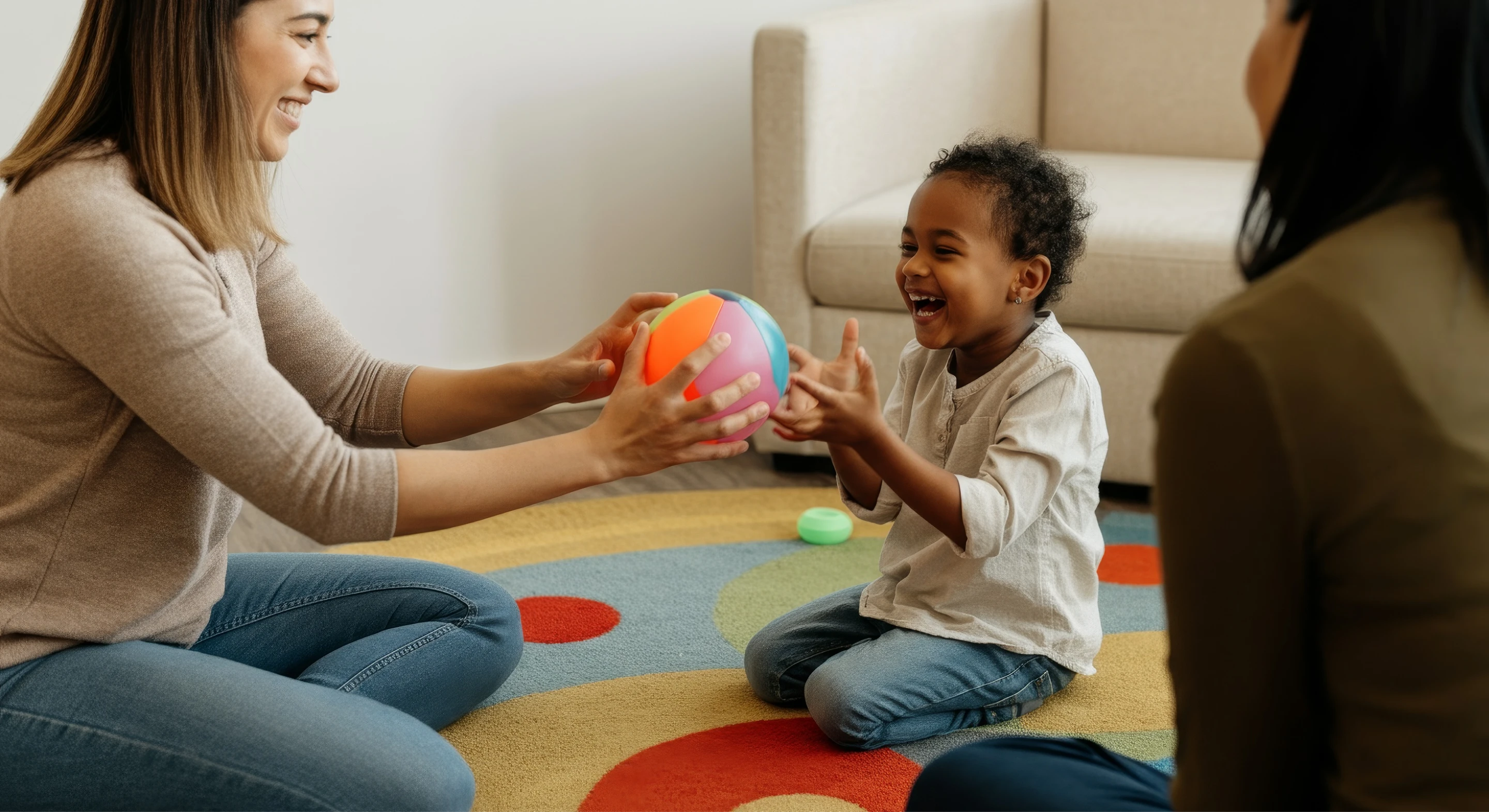 Two women therapists sitting on the floor with a toddler, engaging in interactive play therapy with colorful toys in a warm, supportive environment