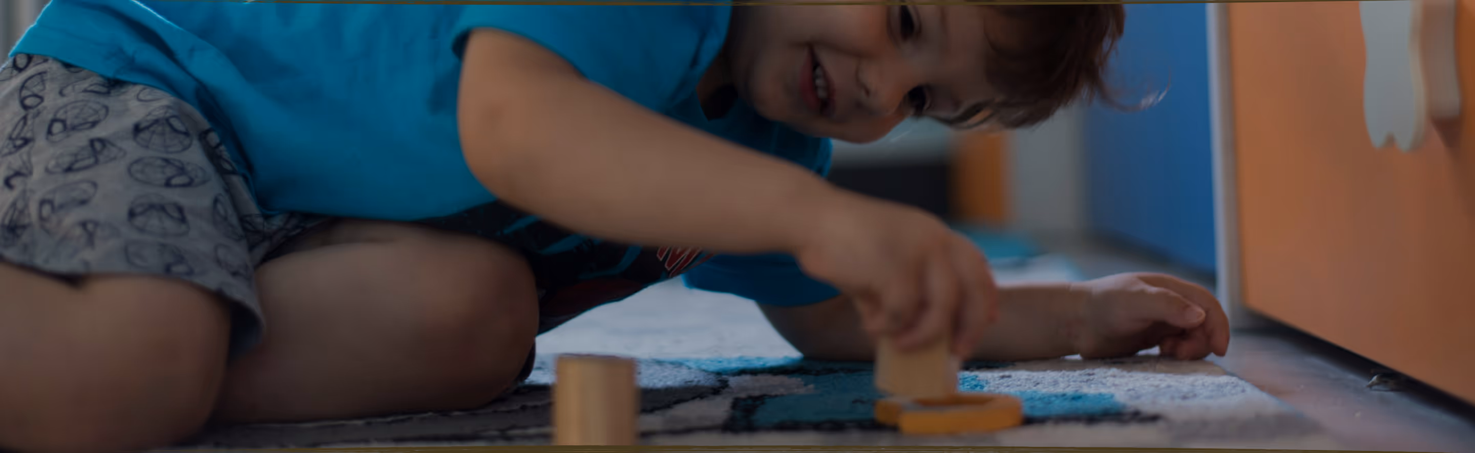 A young child lying on the floor focused on arranging colorful therapeutic stickers, demonstrating concentrated play-based learning activities