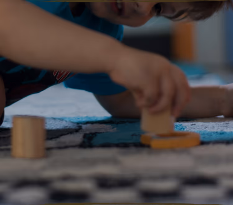 A young child lying on the floor focused on arranging colorful therapeutic stickers, demonstrating concentrated play-based learning activities