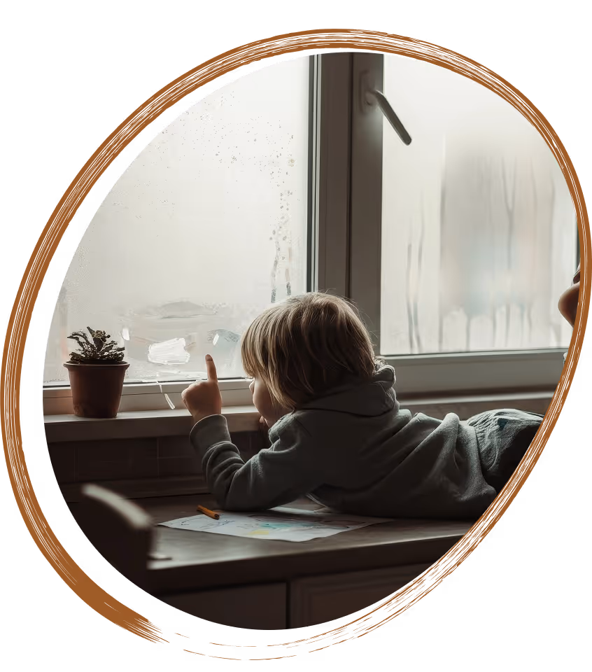 Child sitting by a window on a rainy day, looking outside thoughtfully.