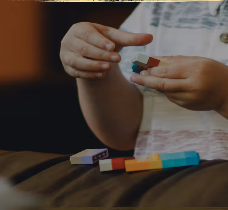 A young child lying on the floor focused on arranging colorful therapeutic stickers, demonstrating concentrated play-based learning activities