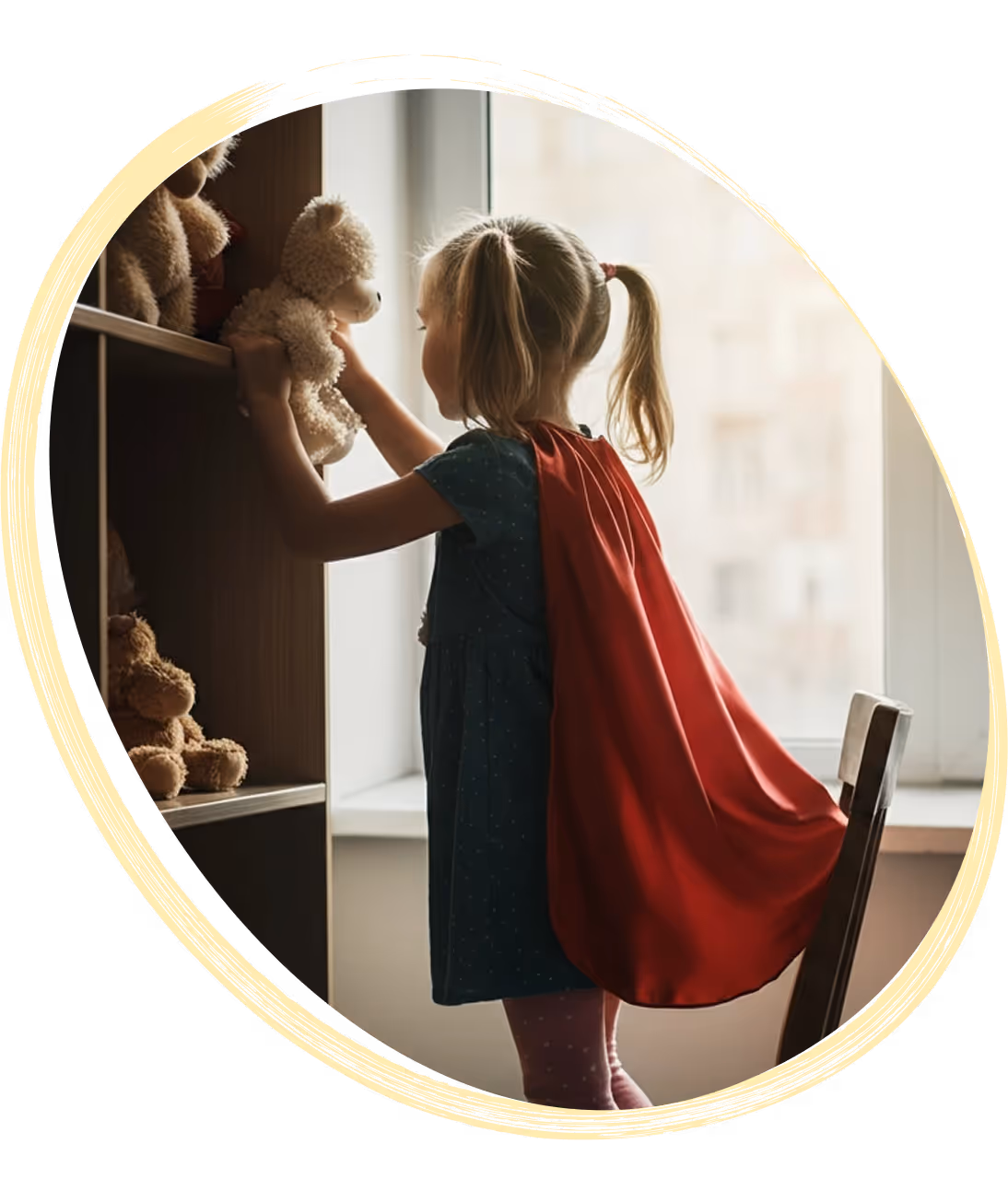 A child wearing a red cape stands by a window, holding a teddy bear, with shelves of stuffed animals nearby.