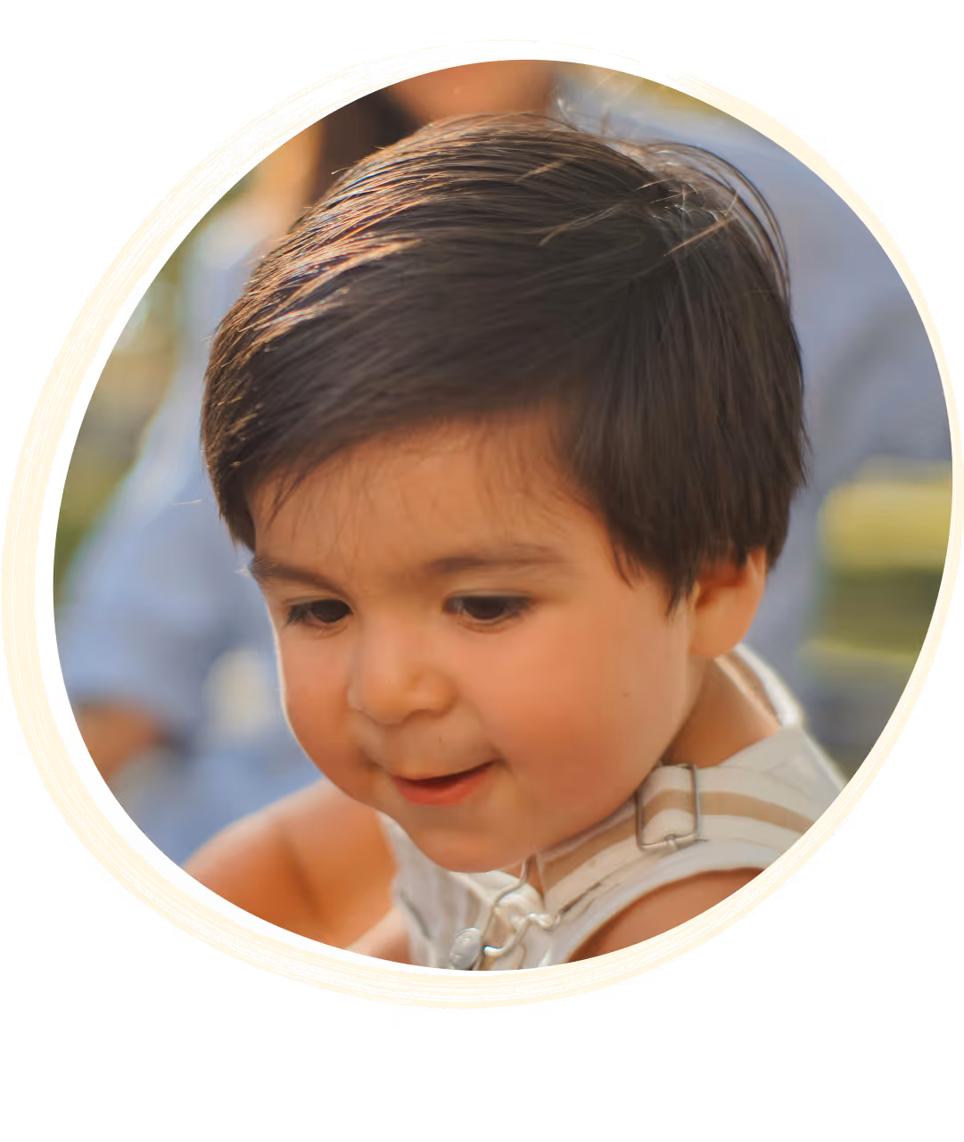 Smiling young boy with short dark hair looking down while playing outdoors.