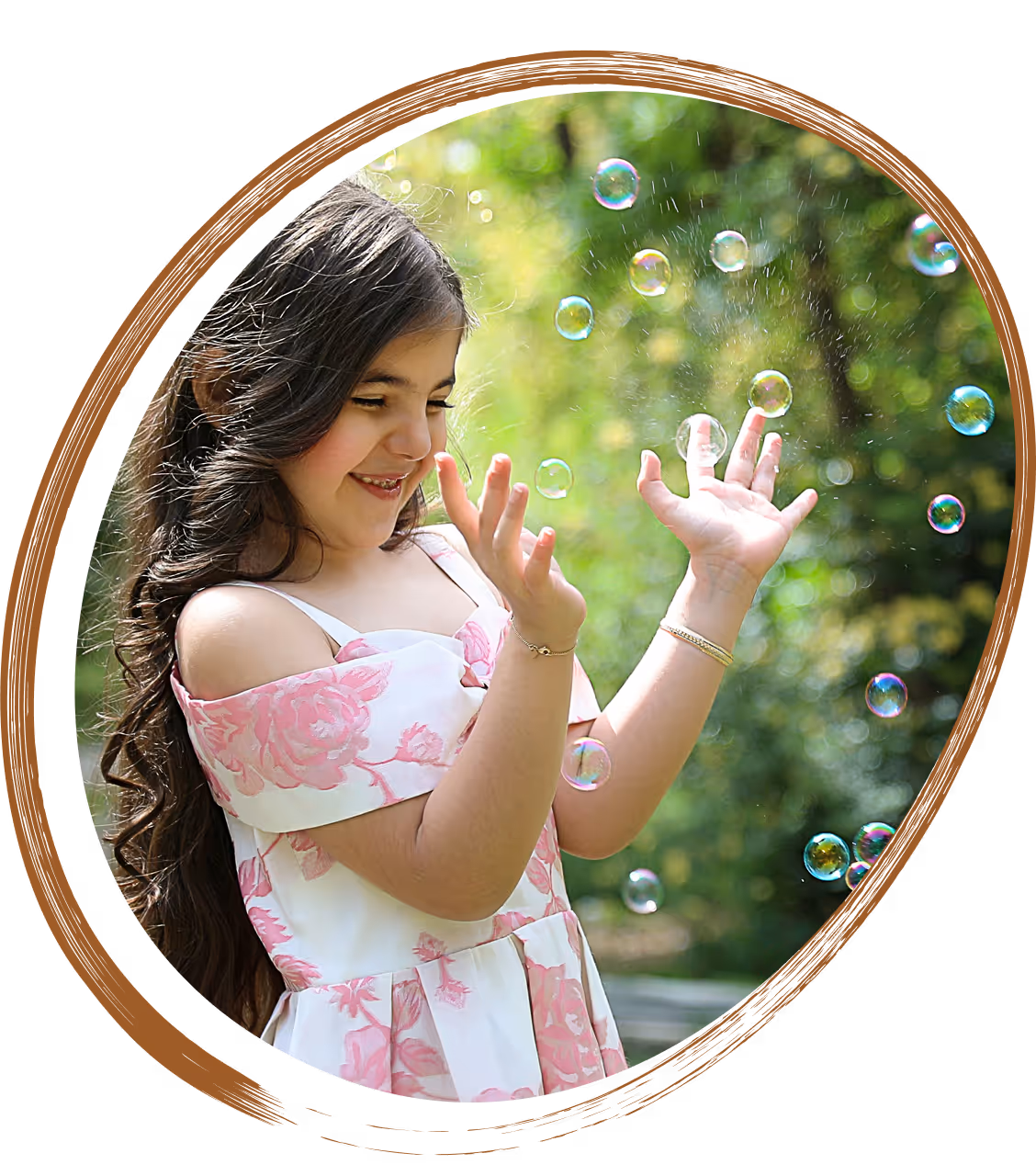 Smiling girl wearing a floral dress playing with soap bubbles outdoors on a sunny day.