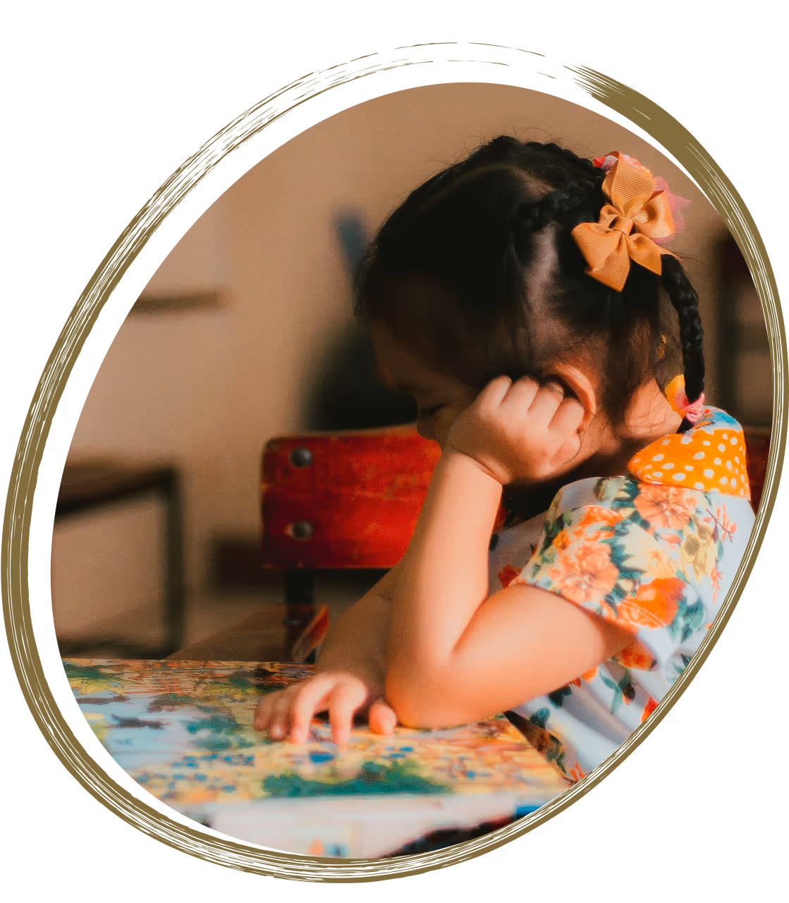 Little girl with braids and a bow sitting at a desk, thoughtfully looking at a colorful storybook.