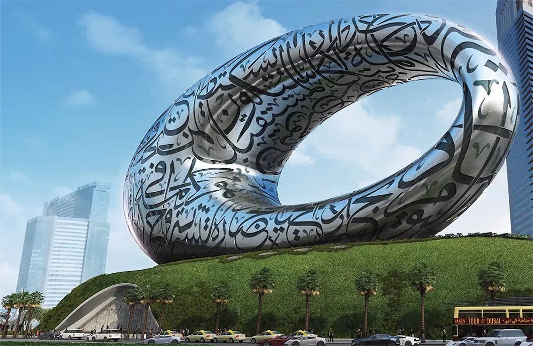 Large hollow, silver oval sculpture, with Arabic inscribed on it. Sitting on top of a building covered in a living wall, with palm trees in front.