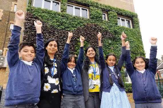 Students in school uniforms celebrating with raised fists in front of ivy-covered building