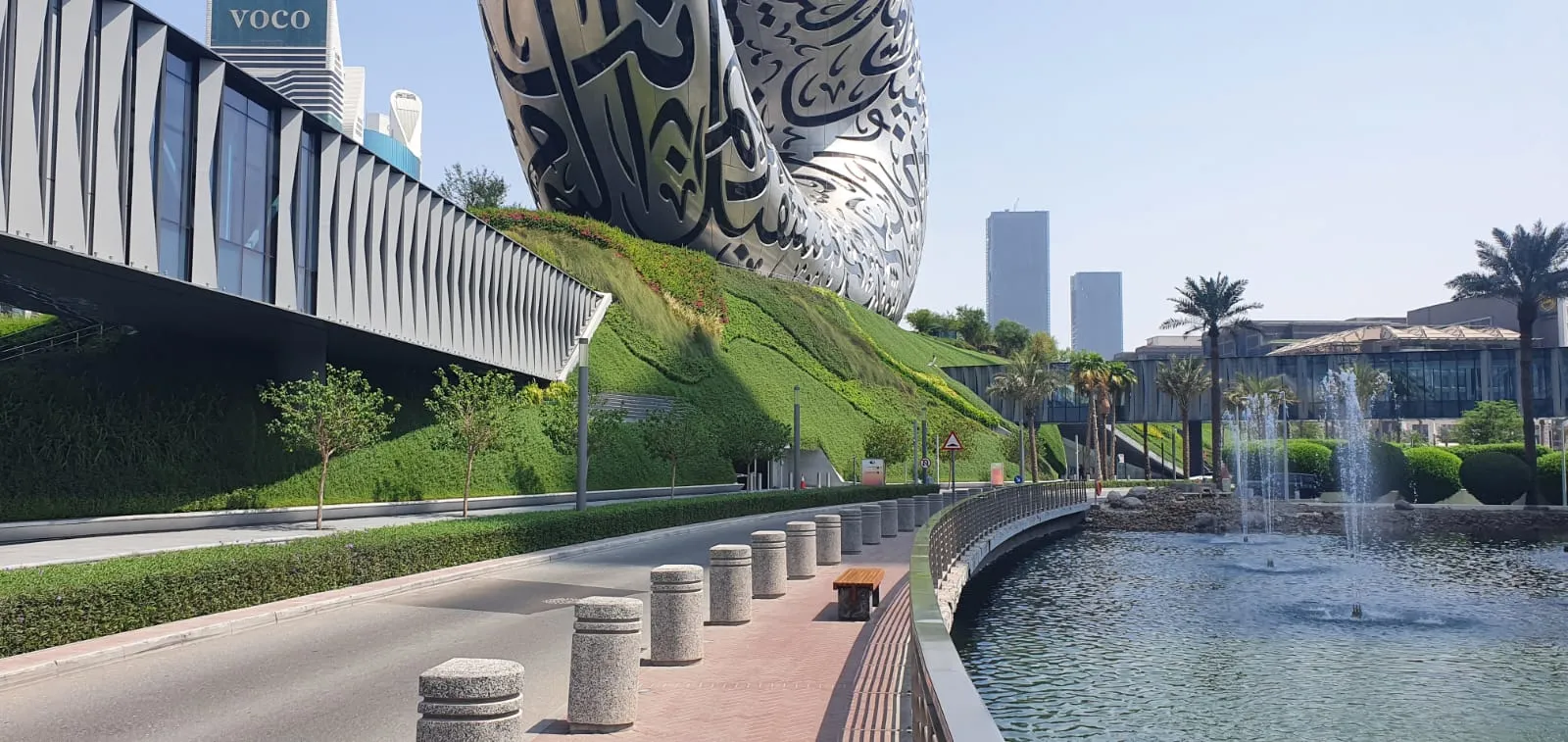 Green hill supporting large, silver structure, in front of large water feature