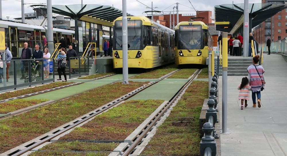Castlefield Metrolink Station in Manchester, where two trains are stopped and between the tracks are spaces of green infrastructure