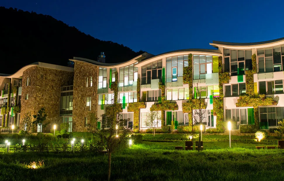 Modern green building complex illuminated at night with mountain backdrop